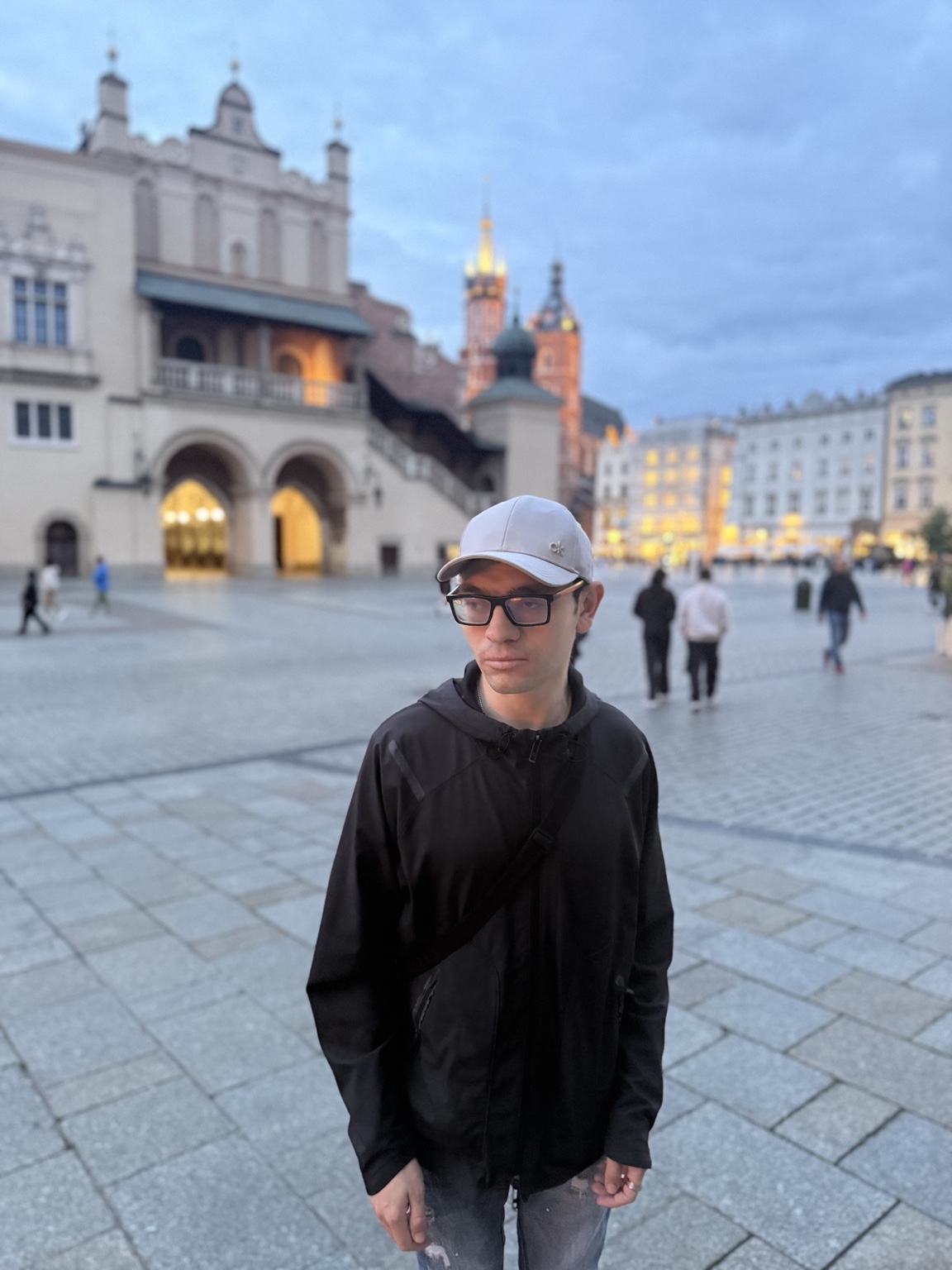 Harry Georgiou wearing a light-coloured cap and dark jacket while standing in a city square
